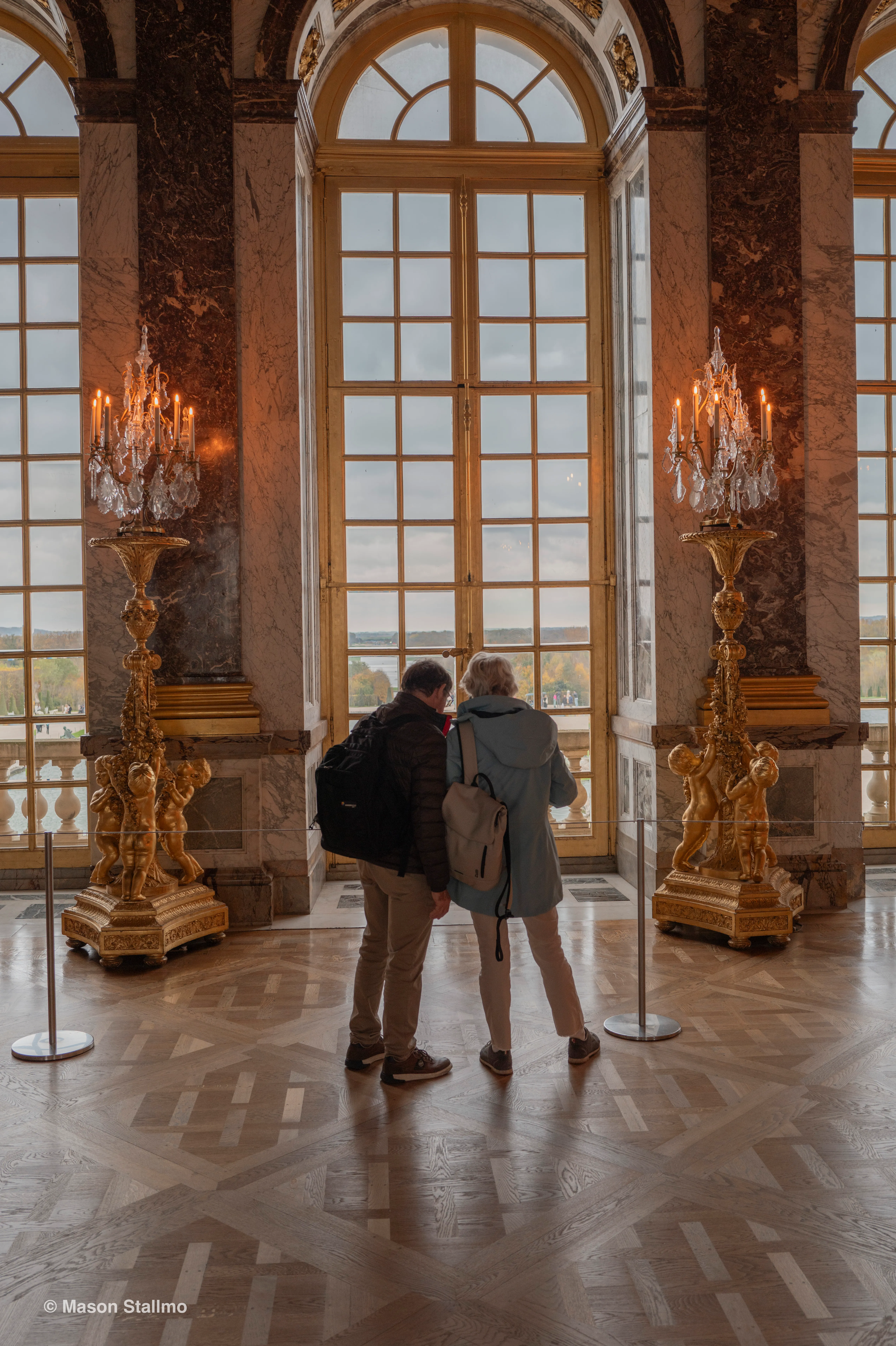 A couple standing in the hall of mirrors looking out a window