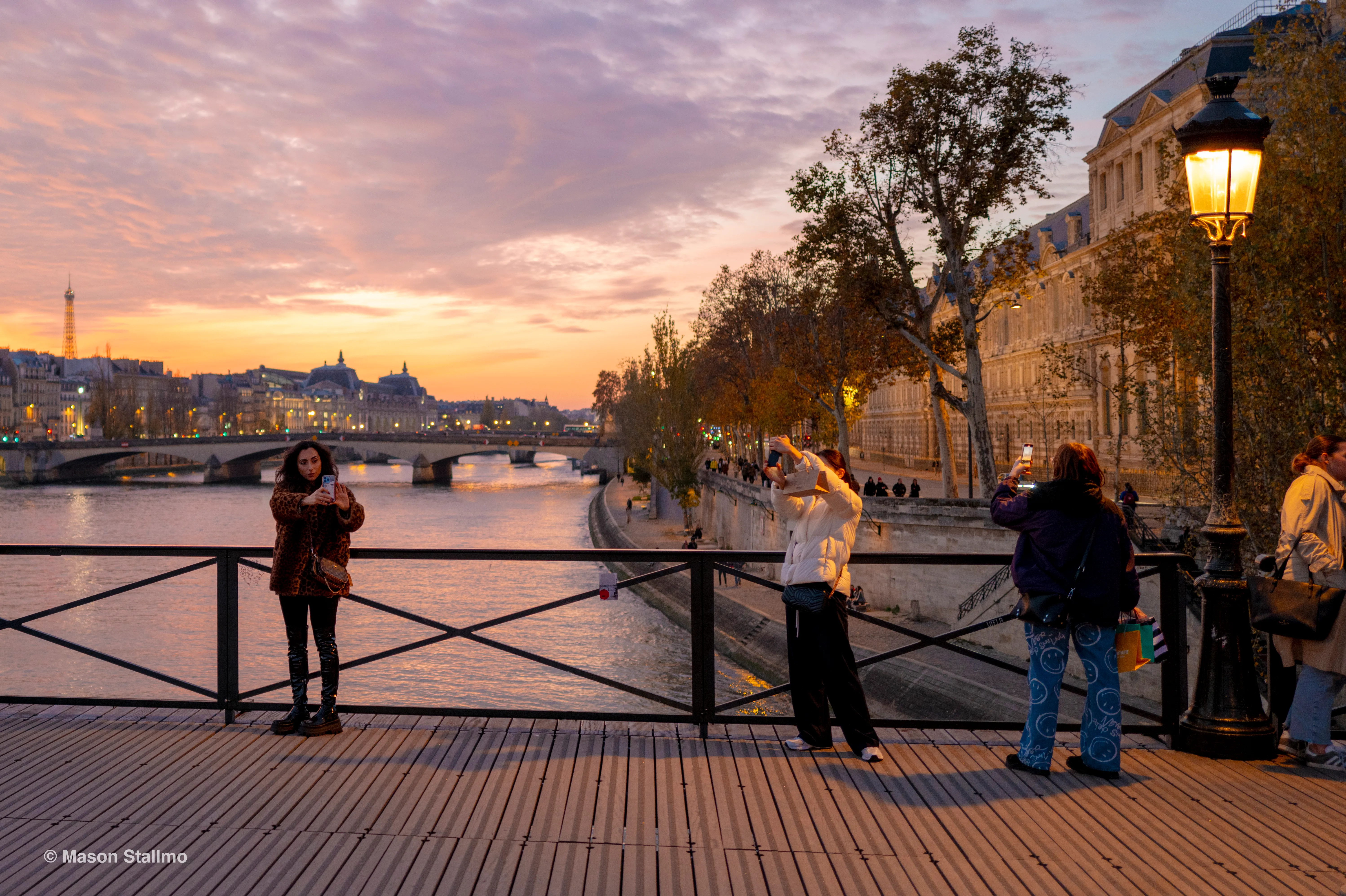 People standing on a bridge over the Siene river taking pictures at sunset